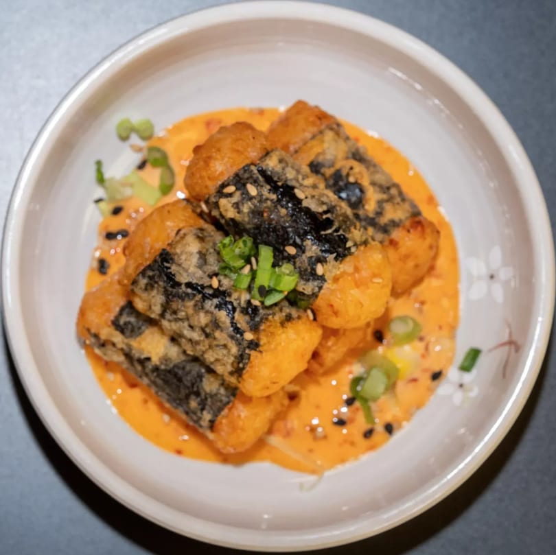 Fried Korean seaweed rolls (gimmari) in a creamy orange sauce, garnished with green onions and sesame seeds.
