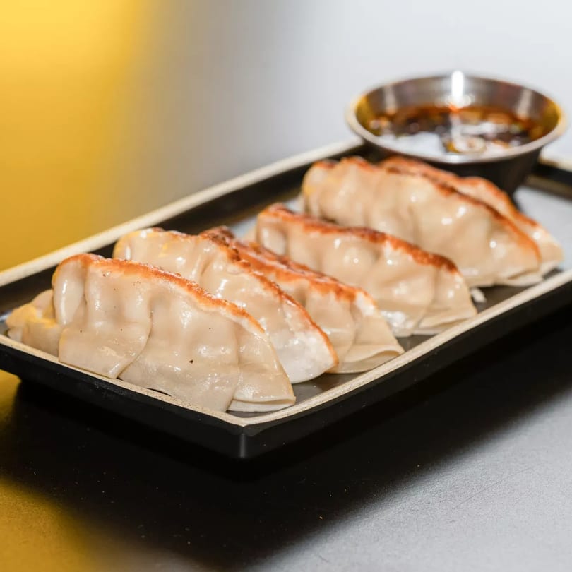 Pan-fried gyoza dumplings with crispy bottoms and a side of dipping sauce on a black rectangular plate.