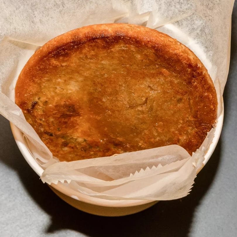 A golden-brown Korean pancake (Hotteok) served in a white paper-lined bowl.