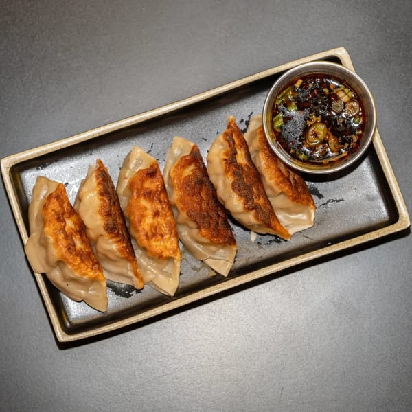 Six pan-fried Seoul Vibez dumplings with crispy bottoms and a side of soy dipping sauce.